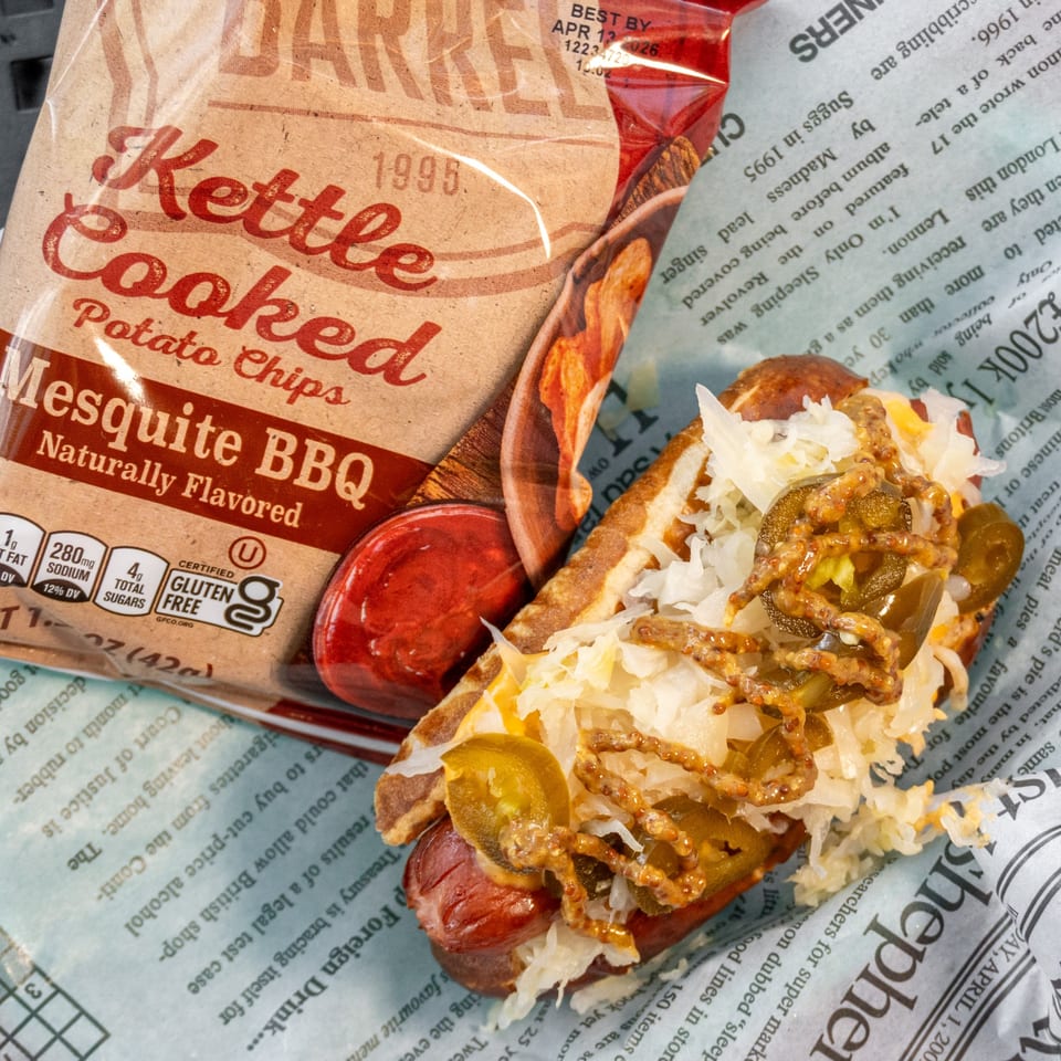 A hot dog with sauerkraut, jalapeños, and mustard, next to a bag of Mesquite BBQ Kettle Cooked Potato Chips.