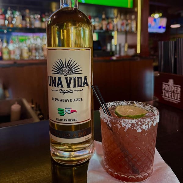 A bottle of Una Vida Tequila next to a red margarita with a lime slice at O'Larney's Pub.