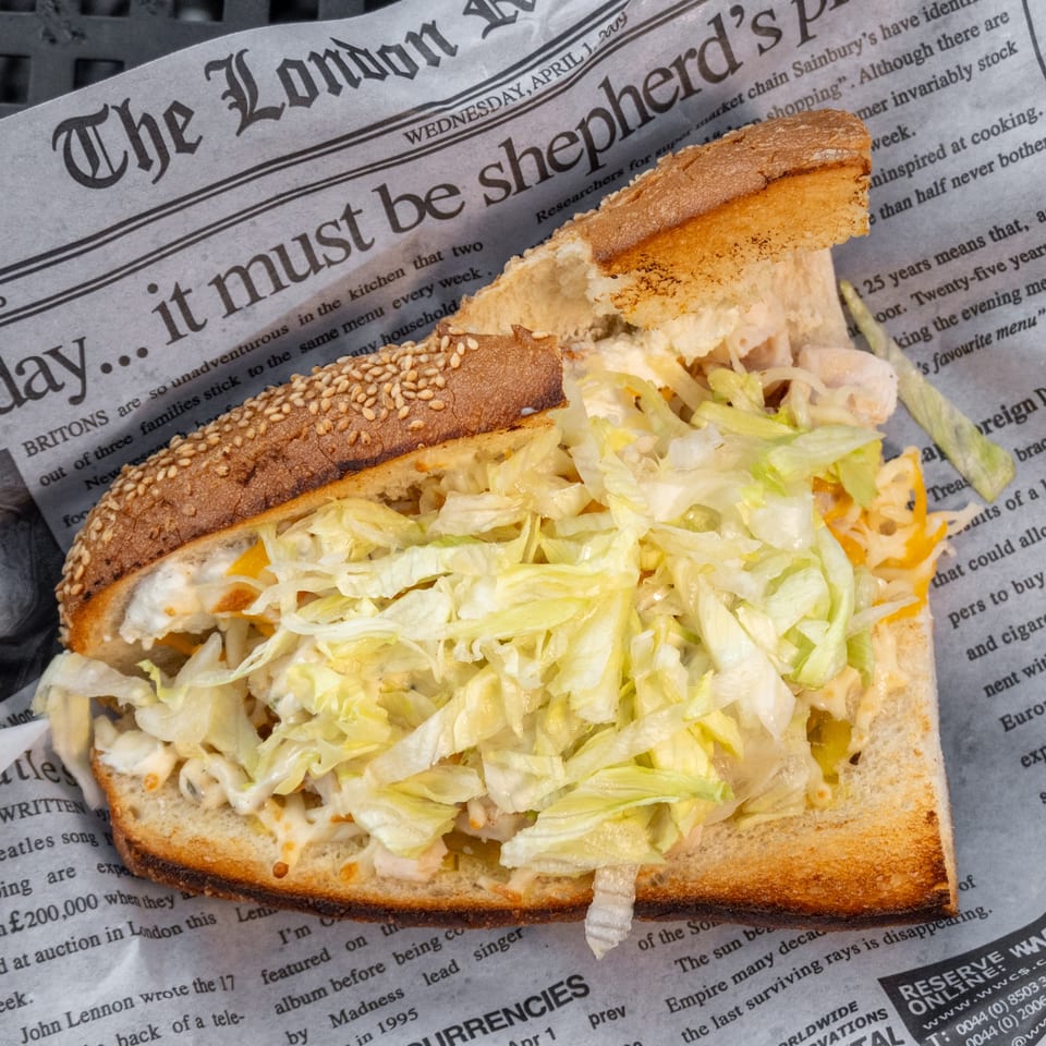 A sesame seed sub sandwich filled with shredded lettuce and cheese, resting on a newspaper.