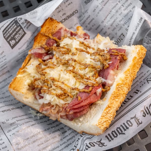 A close-up of a reuben sandwich with corned beef, sauerkraut, and mustard drizzle on toasted bread.