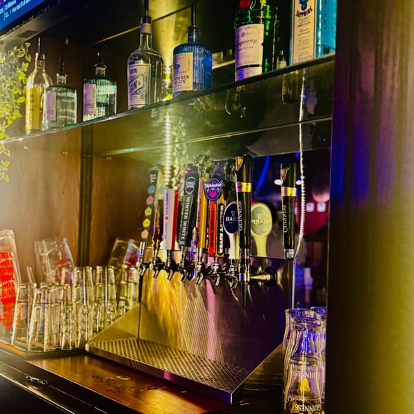 A bar with multiple beer taps, liquor bottles on shelves, and stacks of empty glasses.
